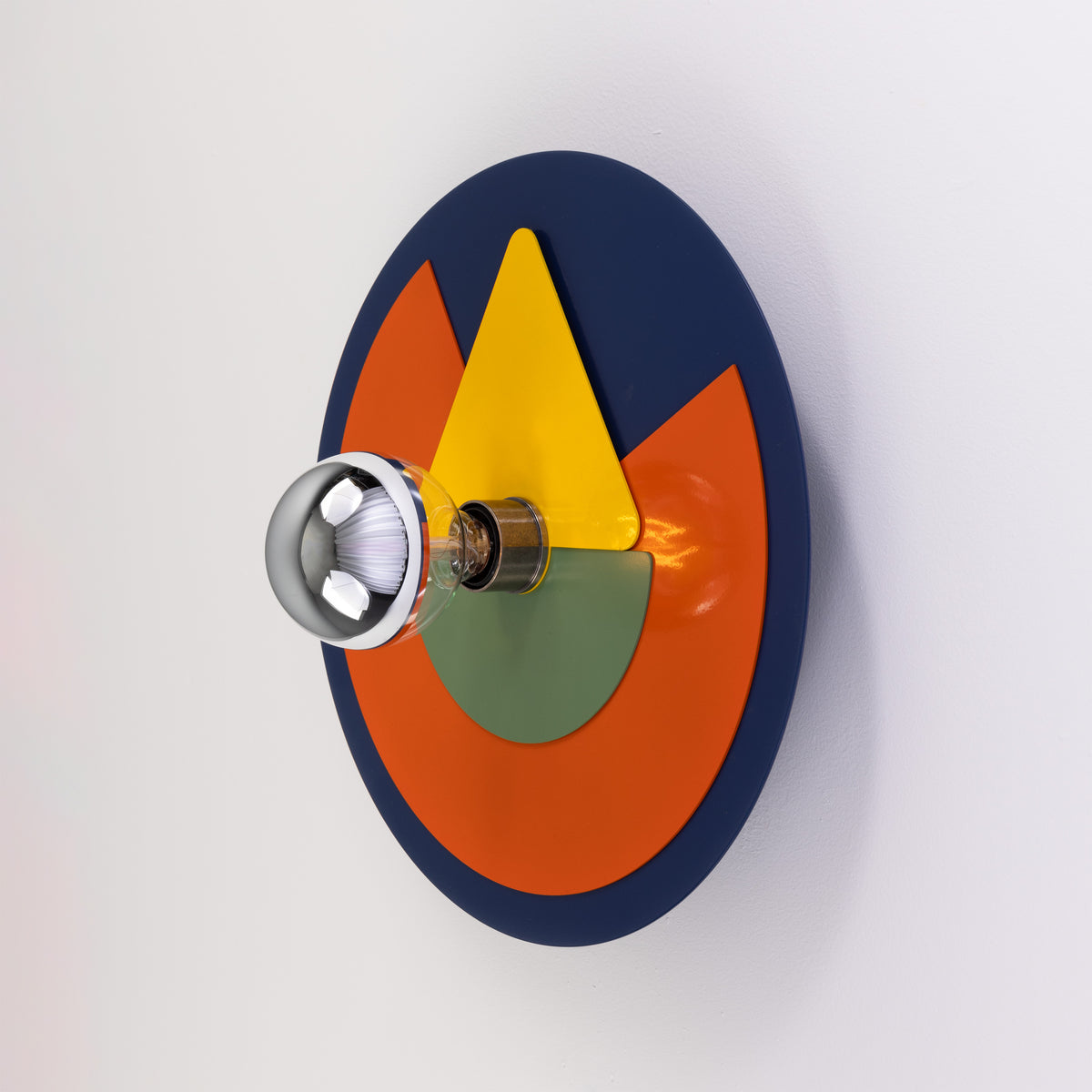 Round wall lamp with blue orange yellow and green geometric metal plates and a silver tipped light bulb