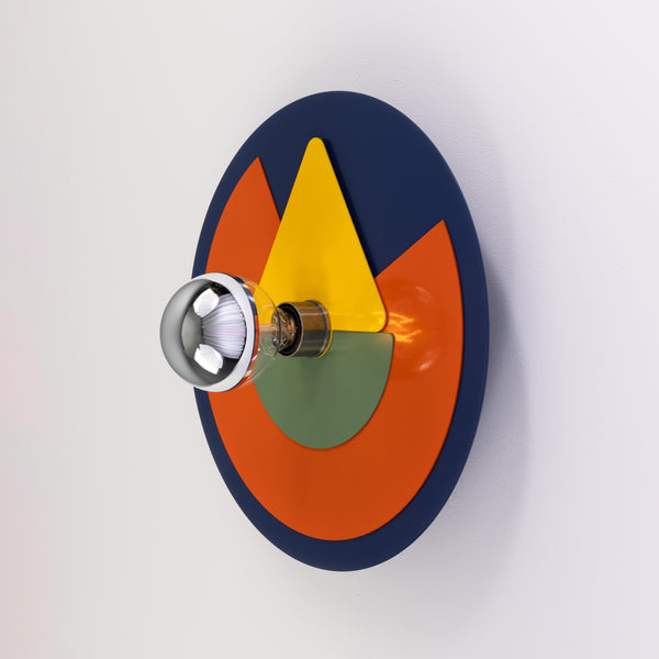 Round wall lamp with blue orange yellow and green geometric metal plates and a silver tipped light bulb