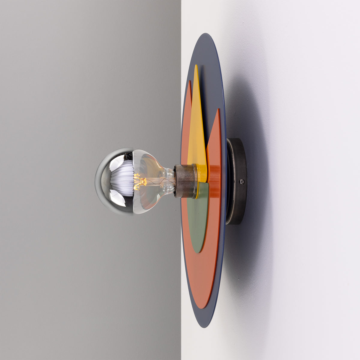 Modern wall sconce with layered circular blue orange and green metal plates and a silver tipped light bulb