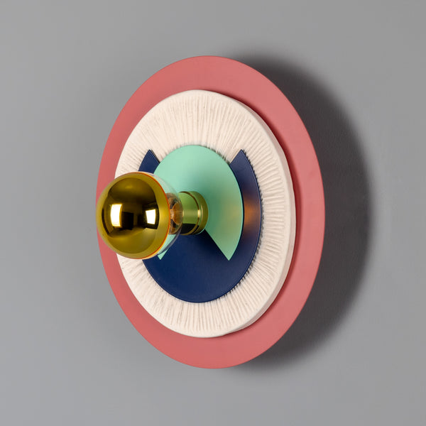 Mullan Saturn colourful disc wall light with a polished brass bulb on a grey wall
