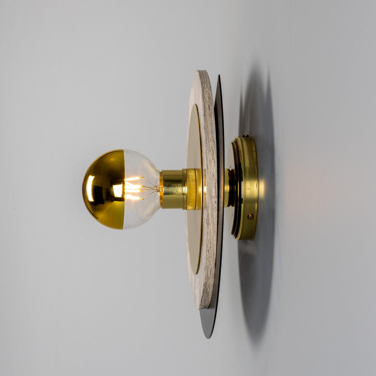 Modern wall sconce with a gold dipped bulb and circular wooden and metal backplate