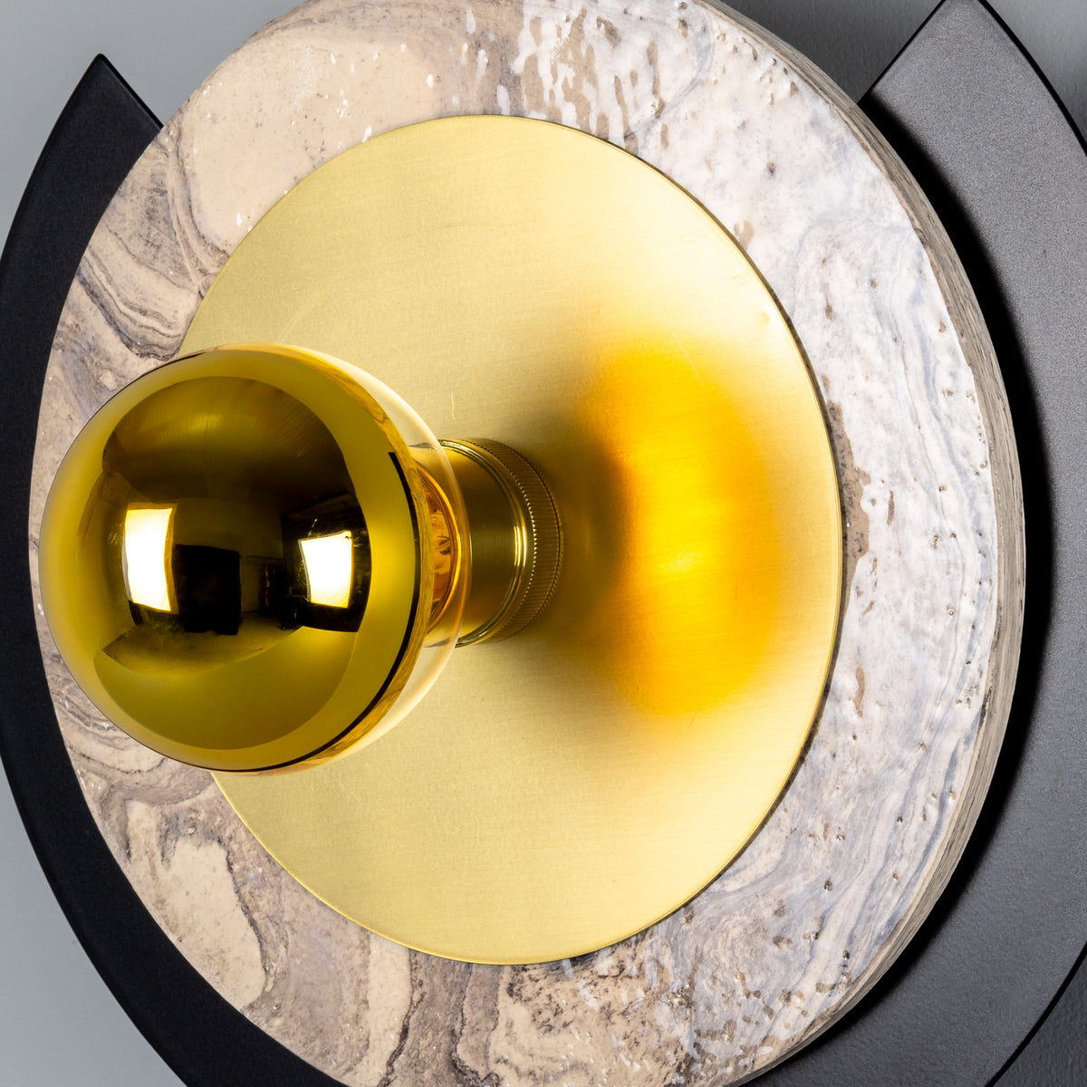 Round wall light with a gold bulb centered on a brass disc and marble backing