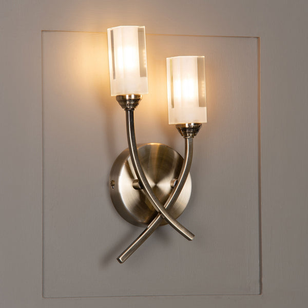 Two-light wall sconce with frosted glass shades and a brushed brass finish.