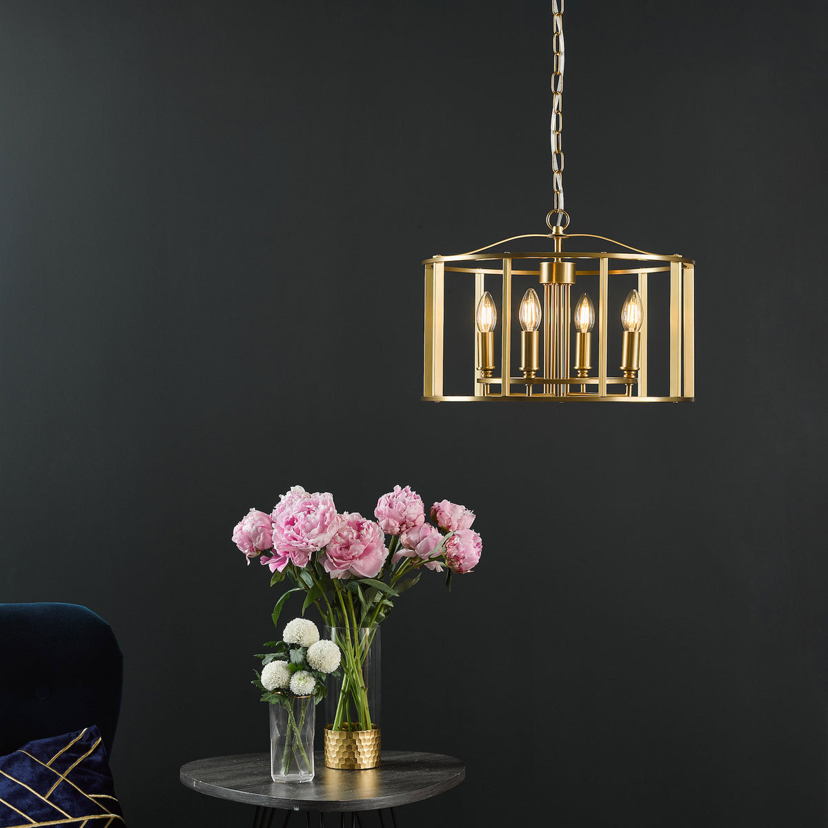 Gold rectangular chandelier with four bulbs, hanging above a table with pink peonies and white flowers.