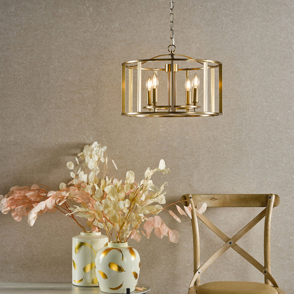 A gold chandelier hangs above two vases with dried flowers and a wooden chair.
