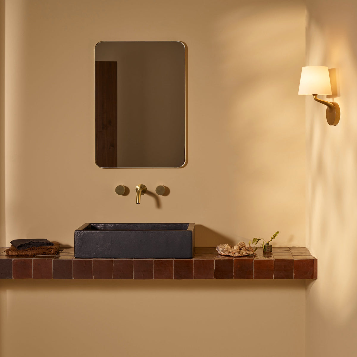 Bathroom vanity with a rectangular mirror, brass faucet, and a dark gray rectangular sink on a tiled shelf