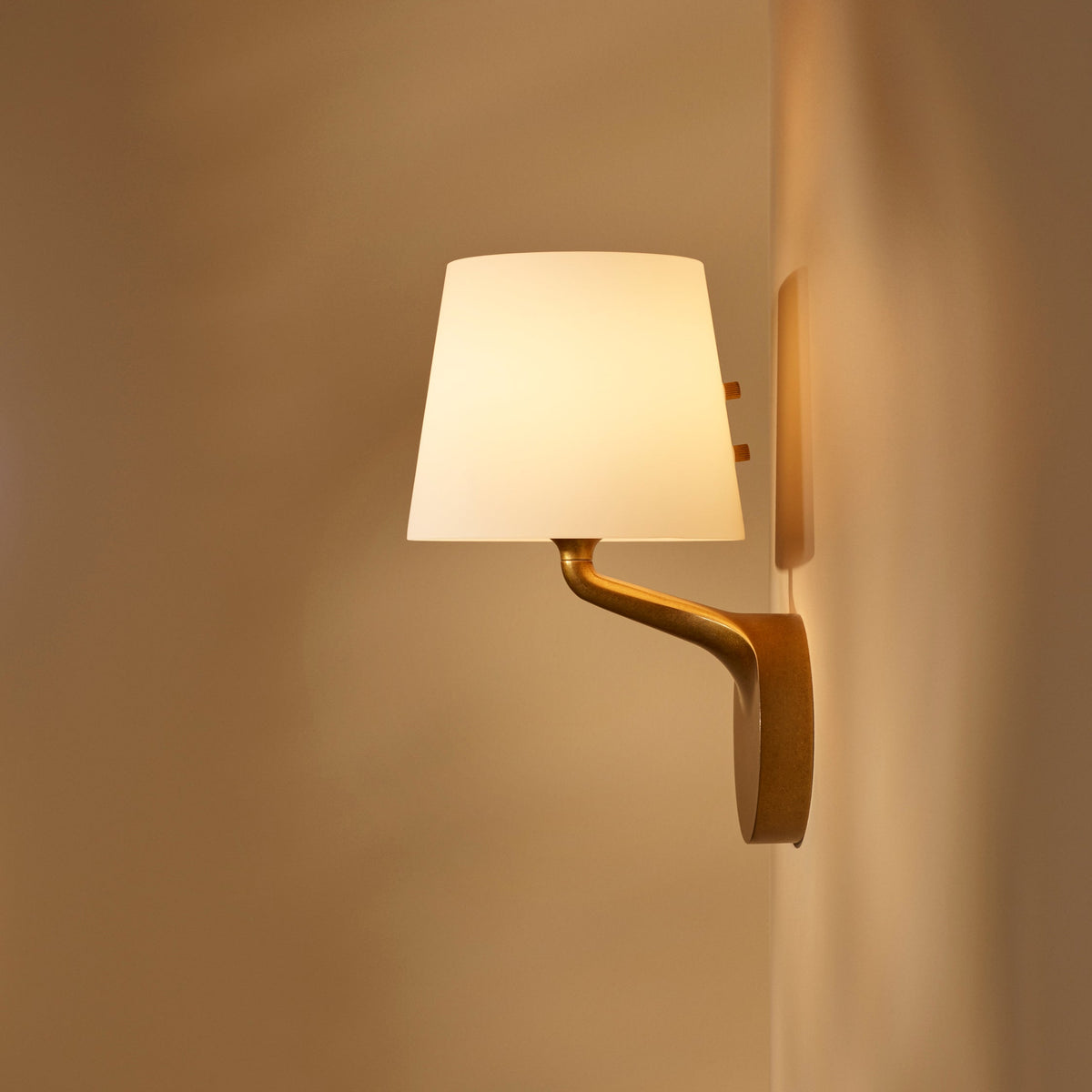 Wall-mounted sconce with a white conical shade and a curved gold-colored arm