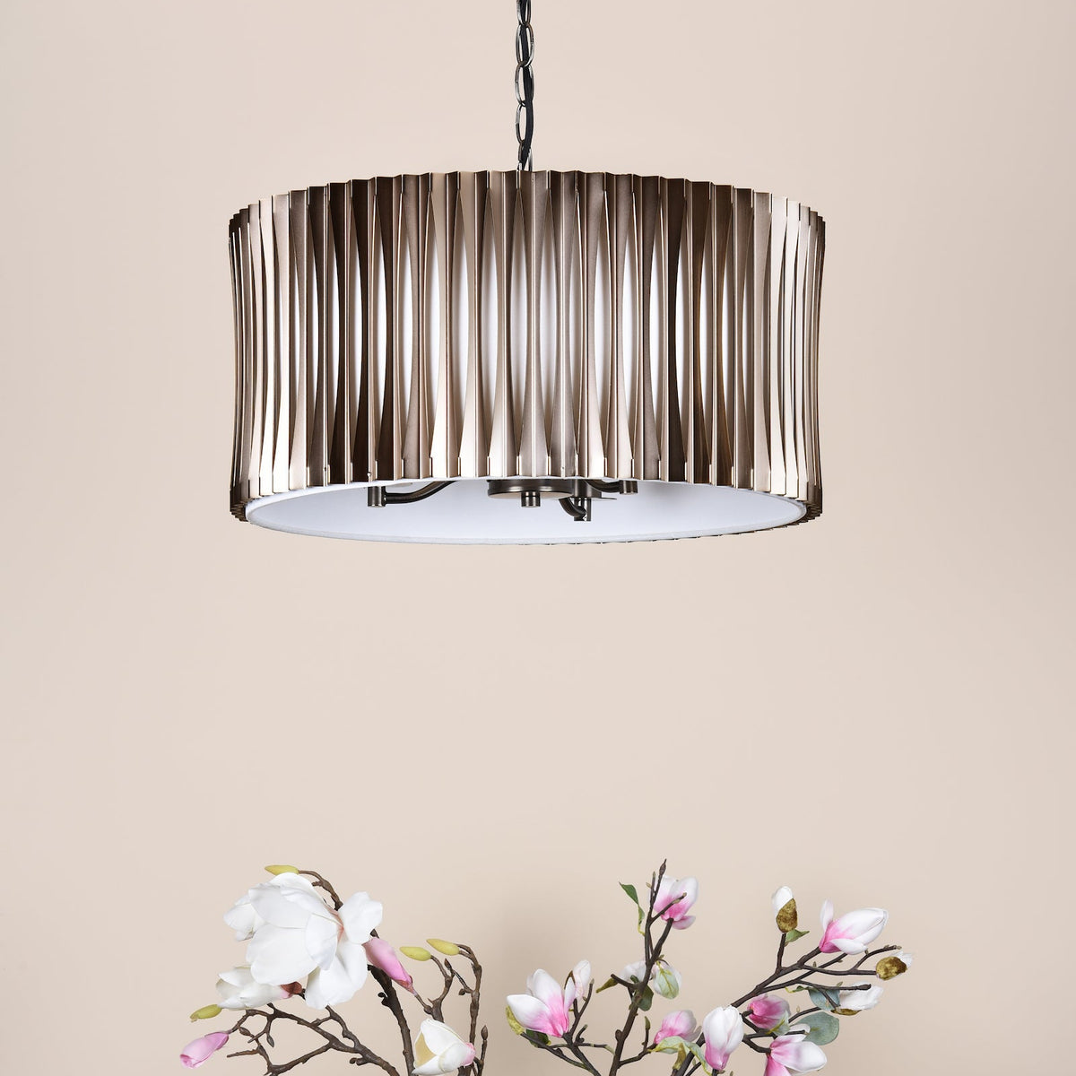 Bronze chandelier with a pleated shade and a white diffuser, hanging above magnolia flowers