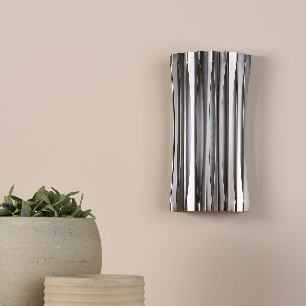 Silver wall sconce with vertical ribbed design and a plant in a pot
