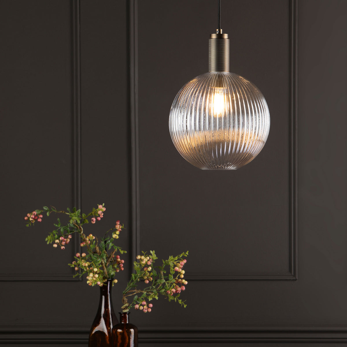 Ribbed glass pendant light with a brass top, illuminating a dark room with decorative wall panels.