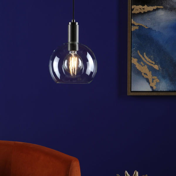 Clear glass pendant light with an Edison bulb, against a dark blue wall with abstract art.