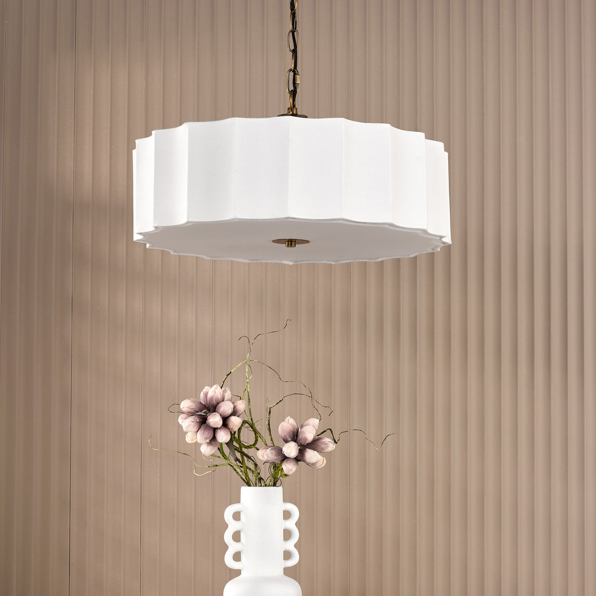 White scalloped pendant light hanging above a white vase with pink flowers and branches