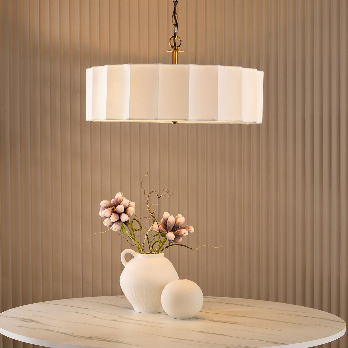 White rectangular chandelier above a round marble table with a white vase of flowers and a white sphere