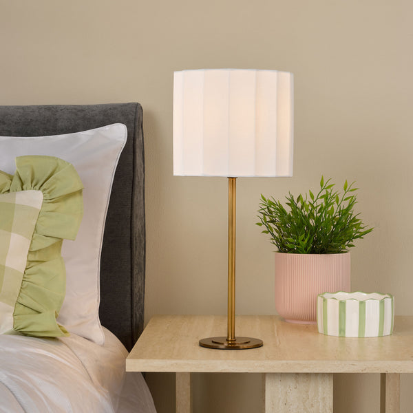A bedside table with a lamp, a plant in a pink pot, and a striped bowl