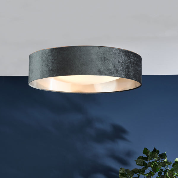 Round ceiling light with a dark green velvet shade and a gold interior, illuminating a dark blue wall
