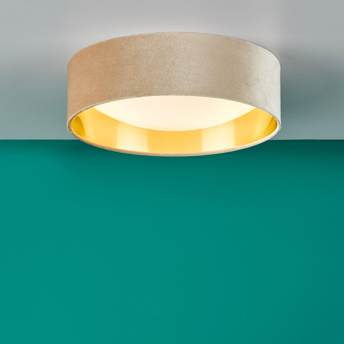 Round ceiling light with a beige fabric exterior and a gold interior, against a teal wall