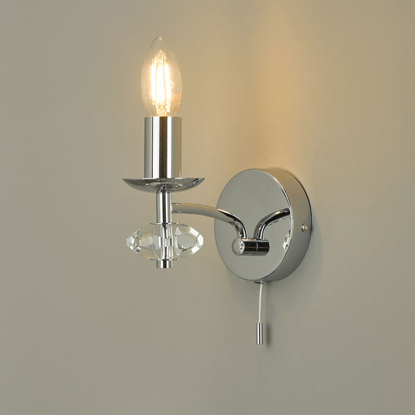 Chrome wall light with a clear crystal-like accent and a pull cord switch, emitting a warm glow.