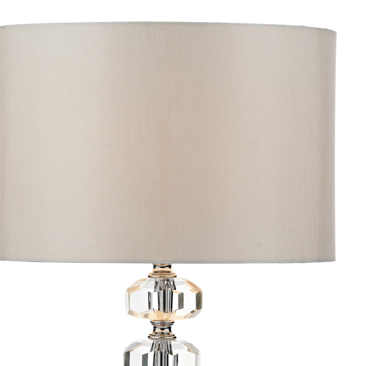 Close-up of a table lamp with a beige fabric shade and a faceted crystal base.