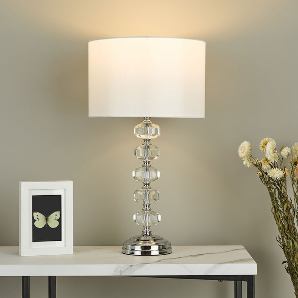 Crystal table lamp with white shade, framed butterfly art, and dried flowers on a marble-top table.