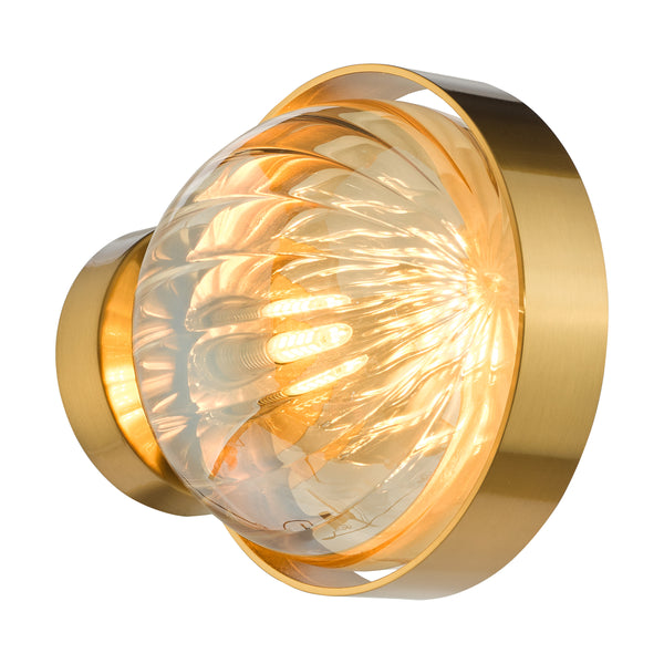 A modern brass wall sconce with a clear, textured glass shade, emitting a warm glow.