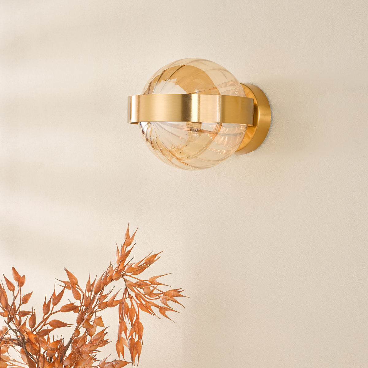 A modern gold wall sconce with a spherical amber glass shade, casting a warm glow on a light wall.