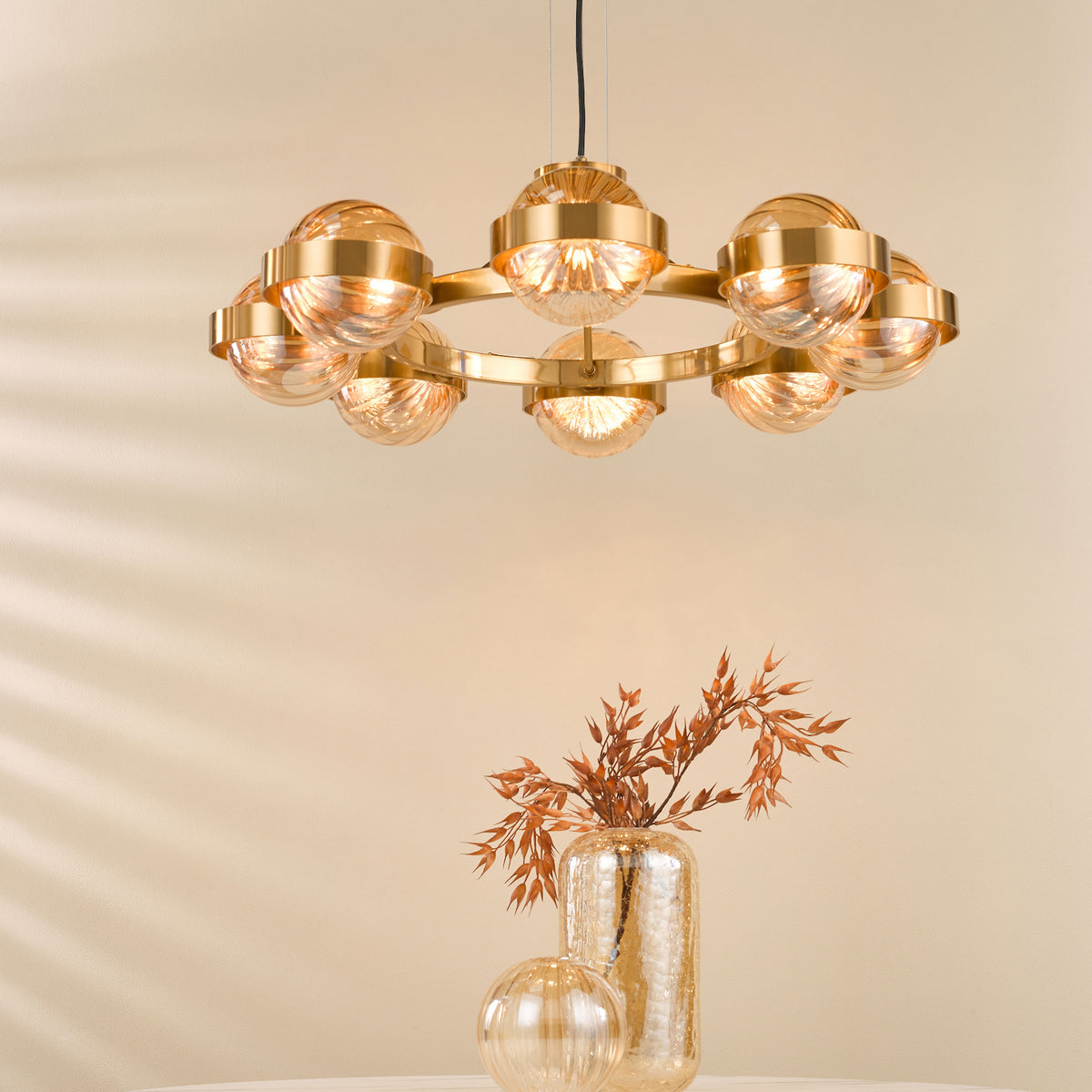 A golden chandelier with round glass shades illuminates a room with a vase of dried foliage.