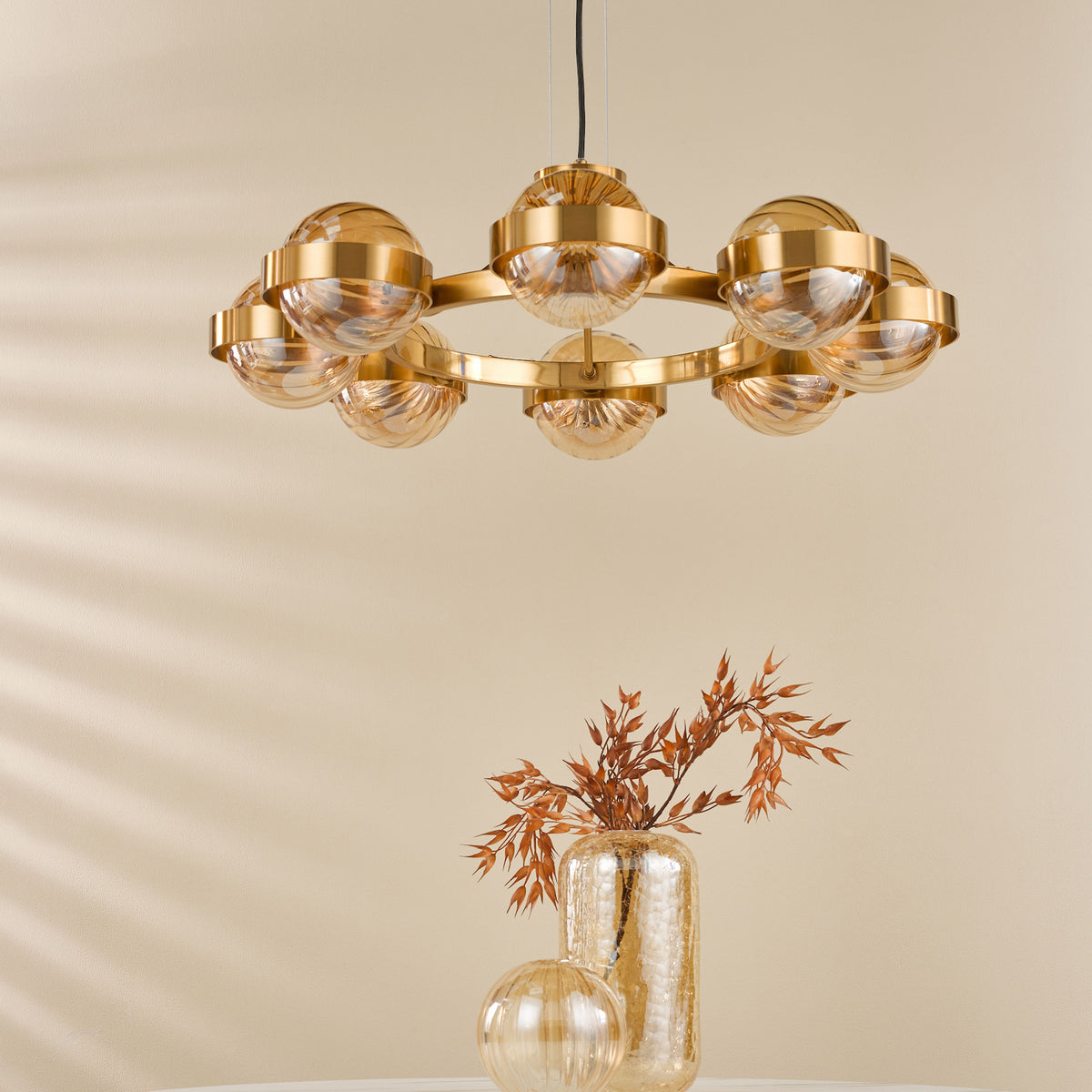 A gold chandelier with eight amber glass globes hangs above a table with two amber vases.