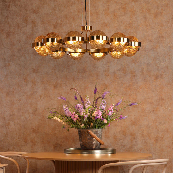 A gold chandelier hangs above a wooden table with a bucket of pink and purple flowers.