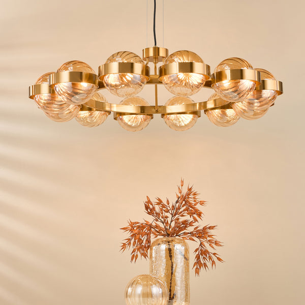 A gold chandelier with amber glass globes hangs above a tall gold vase with dried orange foliage.
