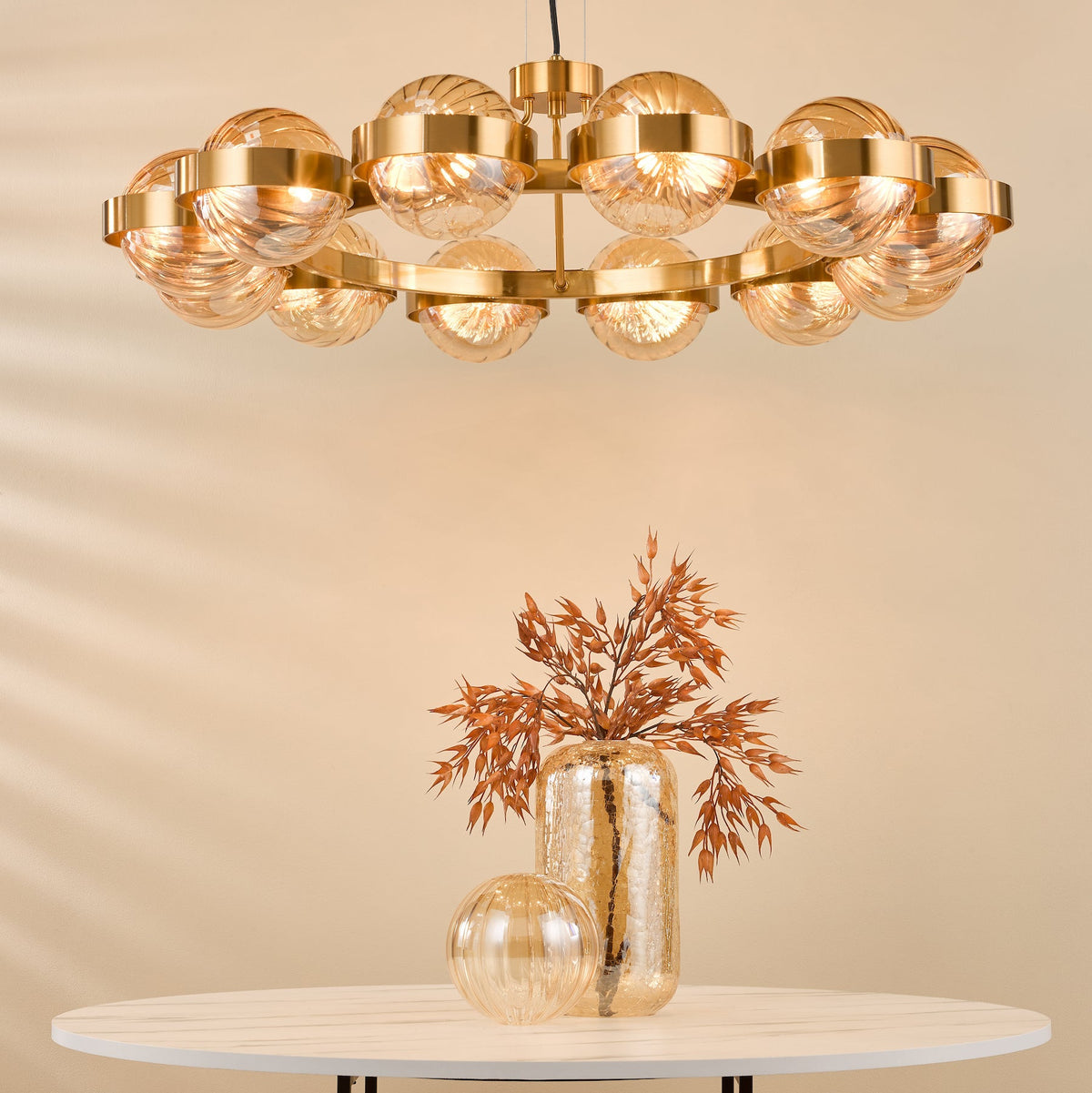 Gold circular chandelier with ribbed glass globes above a white table with a glass vase and dried foliage