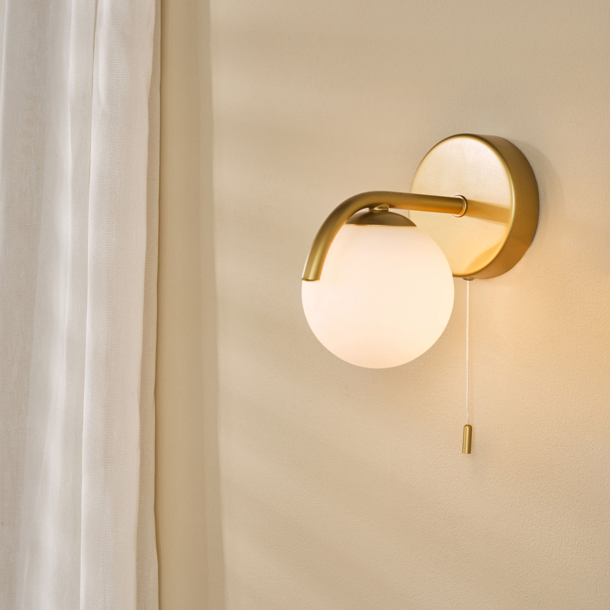 Gold wall sconce with a spherical white glass shade and a pull chain switch