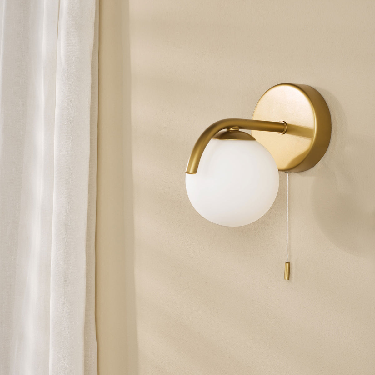 Brass wall sconce with a white globe shade and a pull chain switch