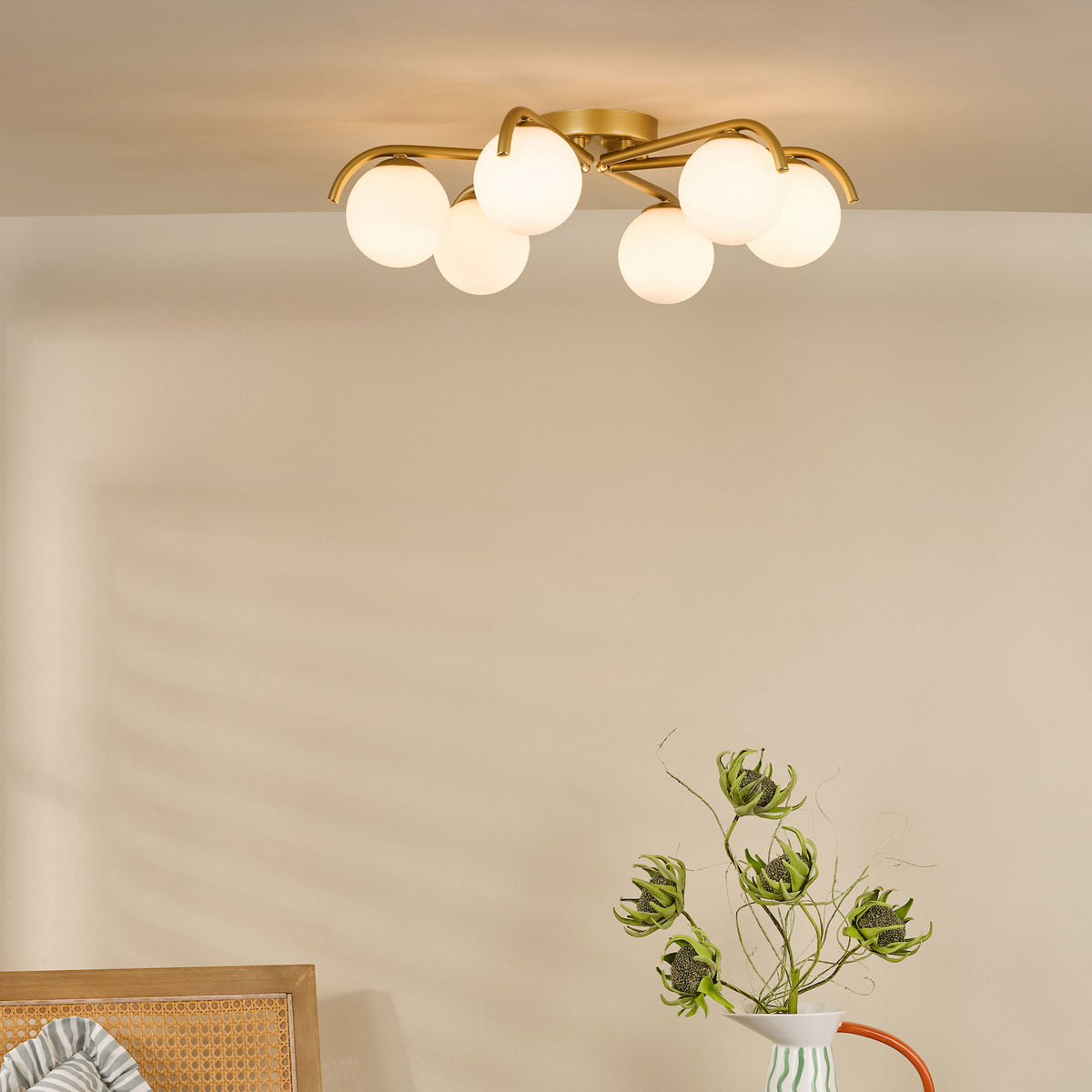 Gold ceiling light with six white globe shades, above a vase with green dried flowers