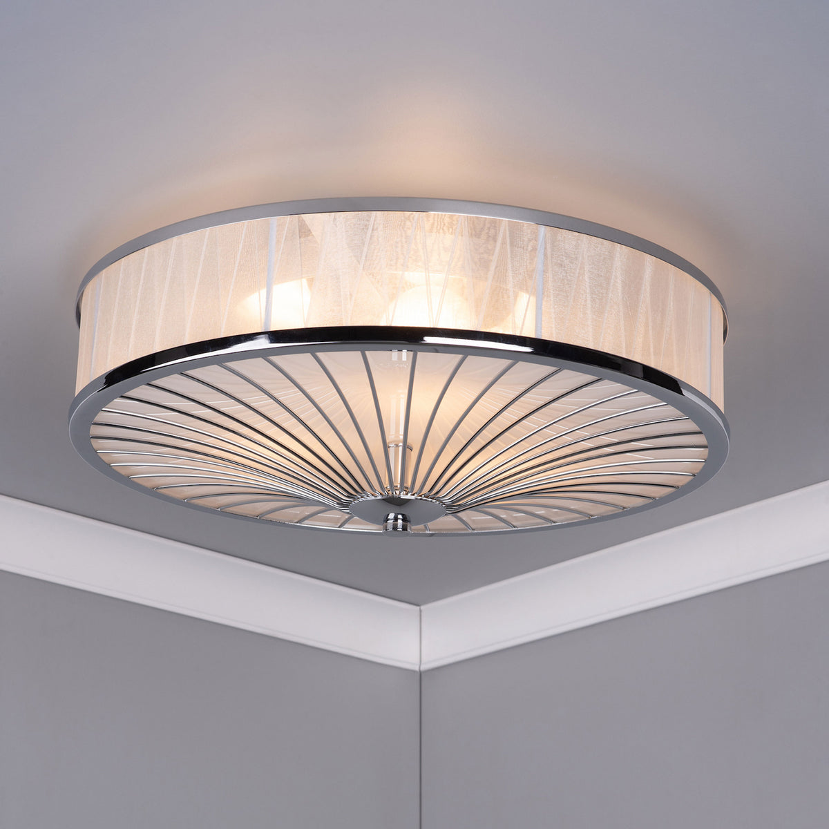 A modern ceiling light with a sheer fabric drum shade and a chrome-finished, fanned metal base.