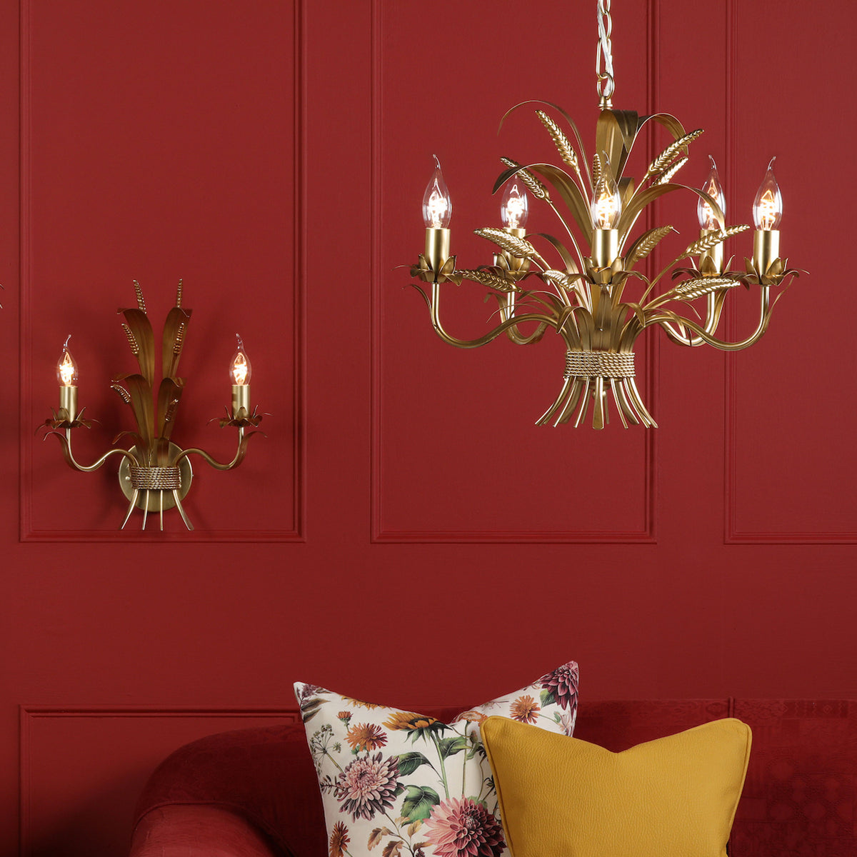 Gold wheat sheaf chandelier and matching wall light on a red wall above a red sofa with cushions