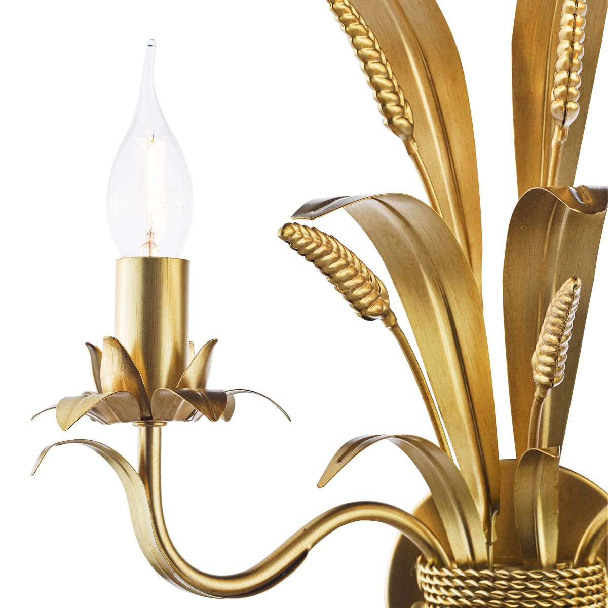 Close-up of a gold wall sconce with a lit candle-shaped bulb and decorative wheat stalks