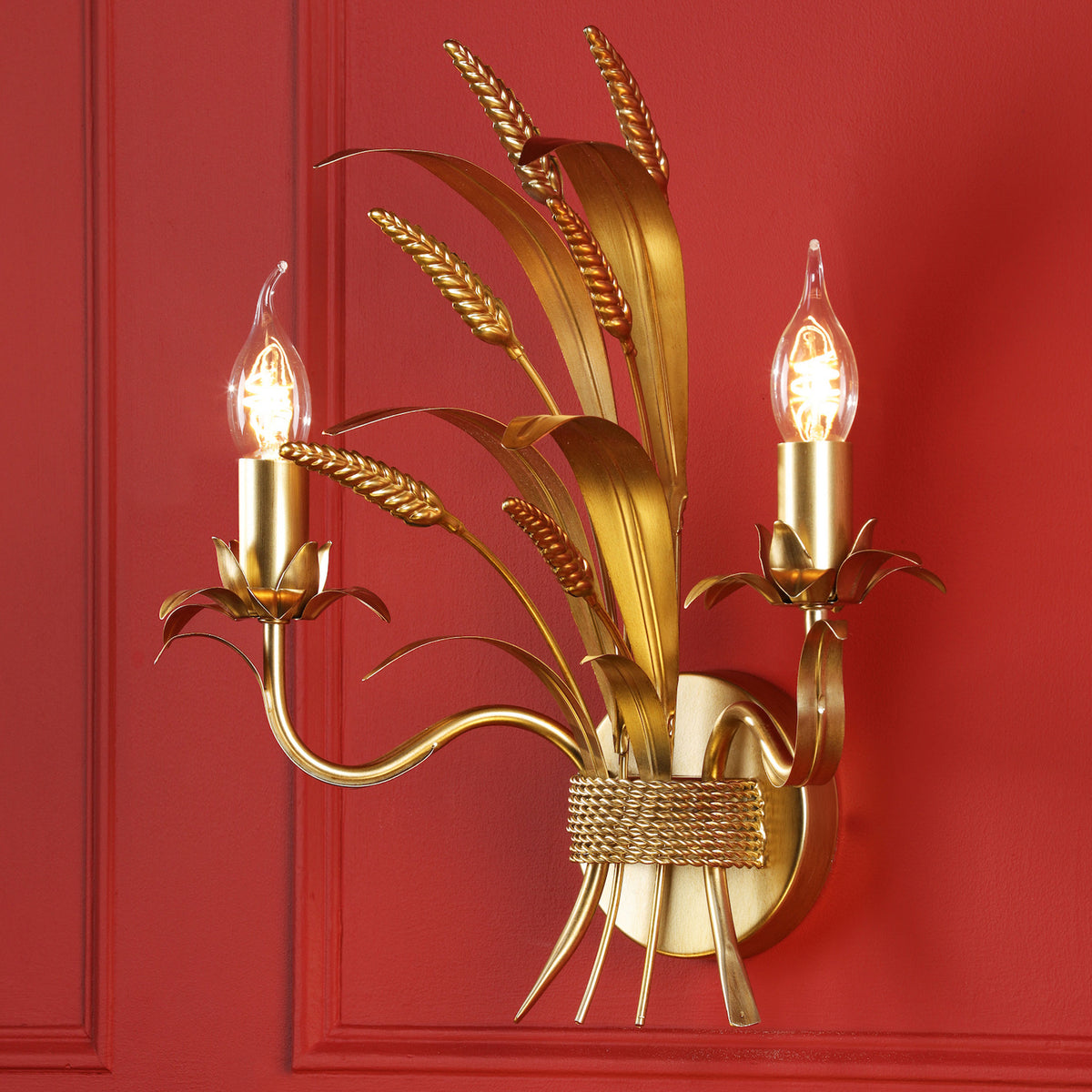 Gold wall sconce with two lights and wheat stalk design on a red wall