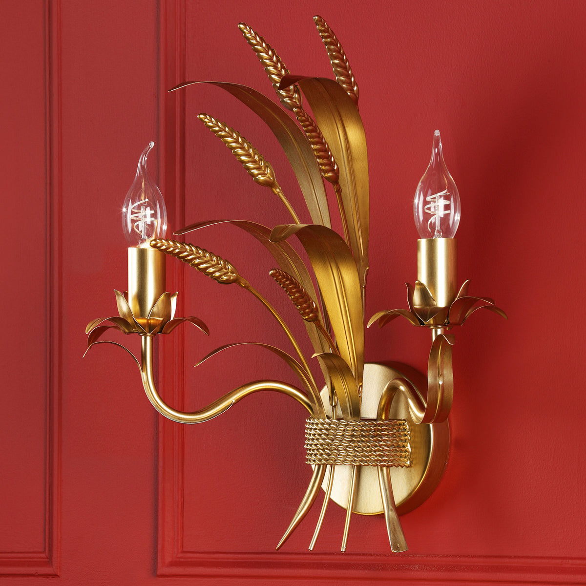 Gold wall sconce with two candle-style bulbs and wheat stalk design on a red wall