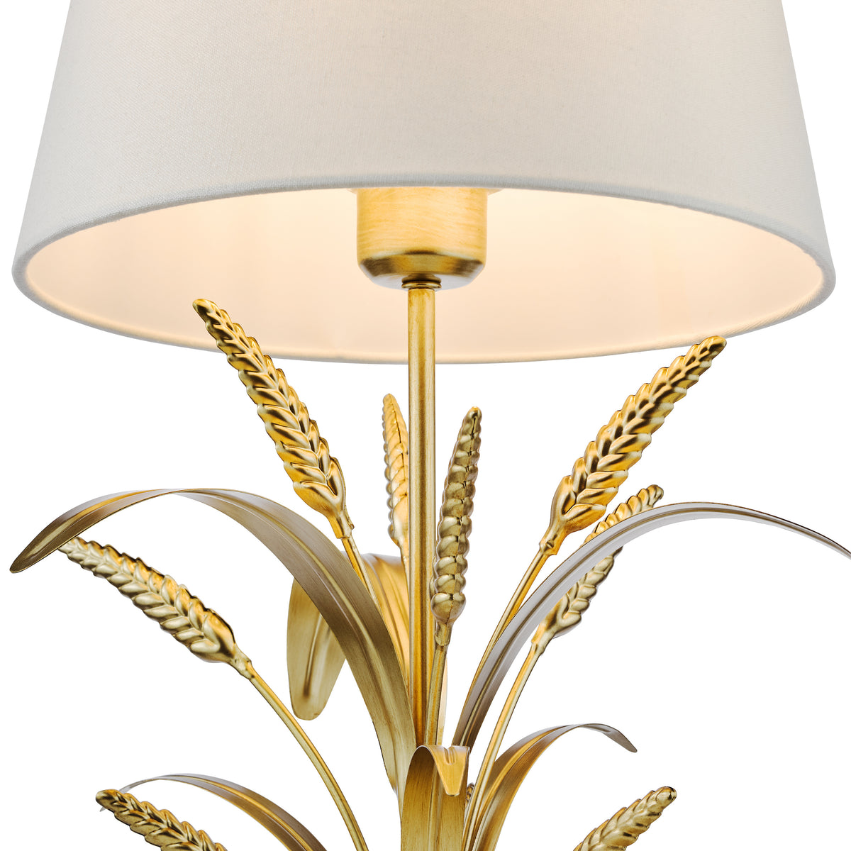 Close up of a gold lamp base with wheat stalk details and a white fabric lampshade