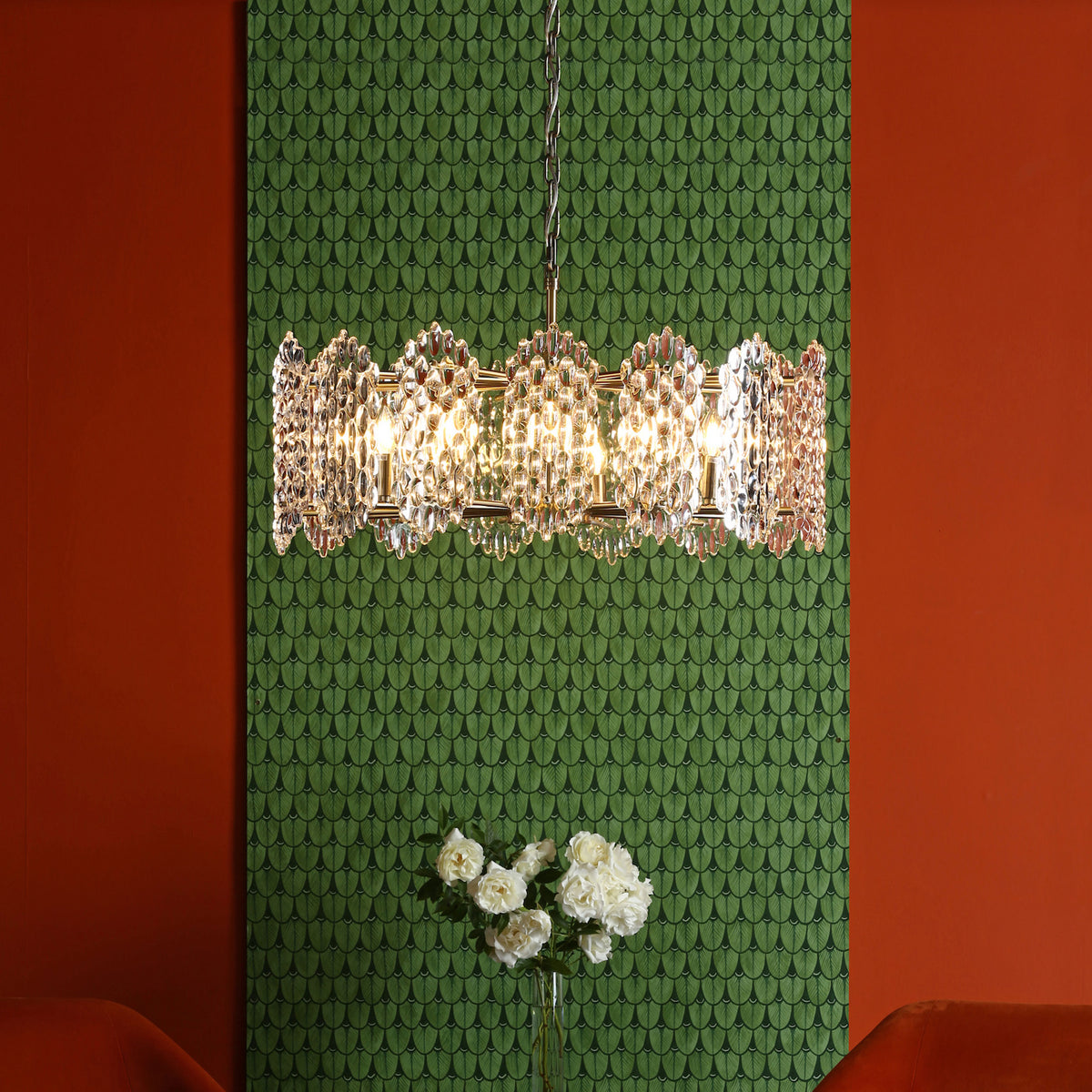 Crystal chandelier with white roses in a vase against a green patterned wall and orange wall