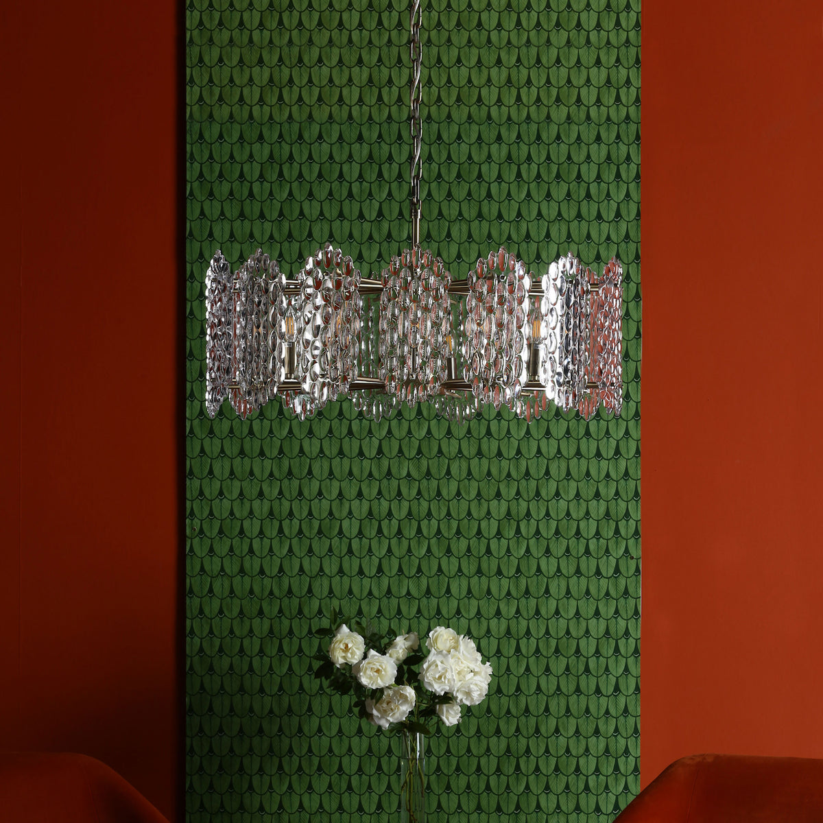 A chandelier with clear glass discs hangs in front of green patterned wallpaper and a red wall