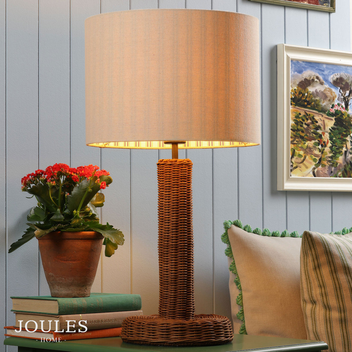 Joules Portree rattan table lamp with a natural linen drum shade on a green table