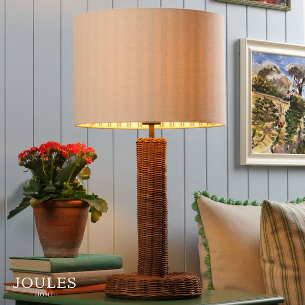 Joules Portree rattan table lamp with a natural linen drum shade on a green table