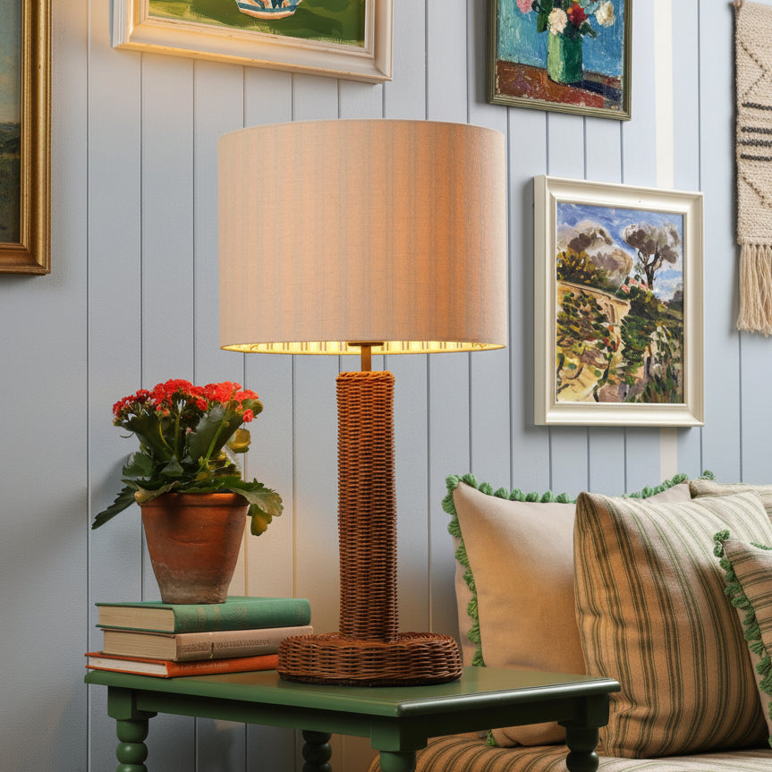 Table lamp with a woven rattan base and a cylindrical fabric shade on a green side table