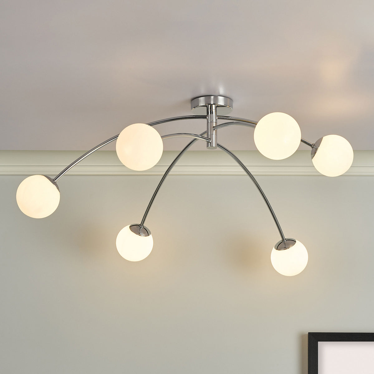 Chrome ceiling light with six curved arms and spherical white glass shades.