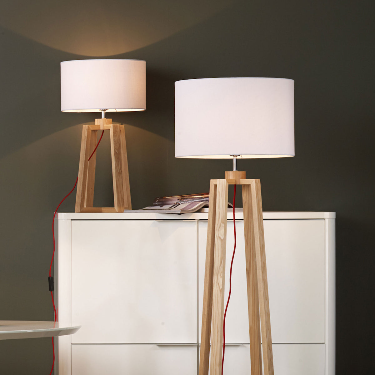 Two wooden tripod lamps with white shades, one floor lamp and one table lamp, on a white cabinet.