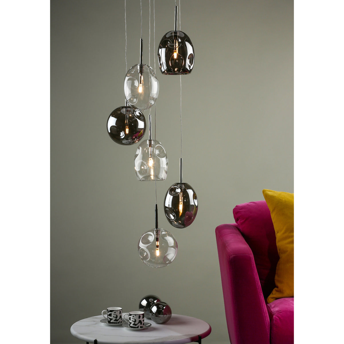 Modern ceiling lights with clear and smoked glass shades hanging above a marble table and pink sofa.