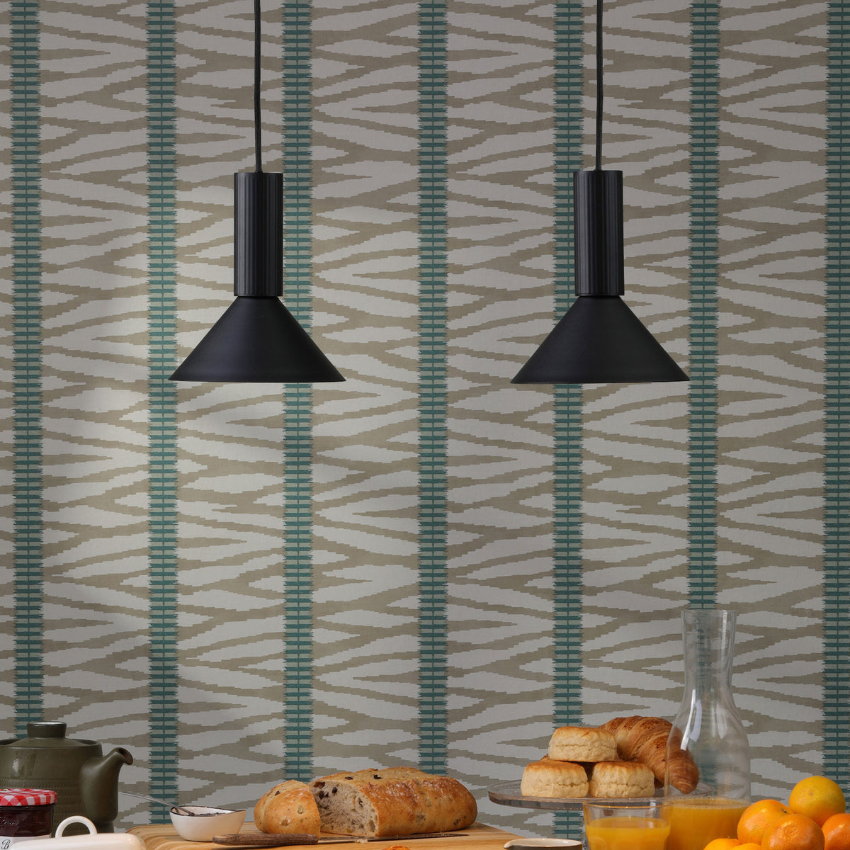 Breakfast table with bread, pastries, orange juice, and a teapot against a patterned wallpaper