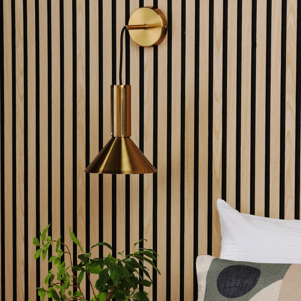 Gold wall sconce with a conical shade mounted on a slatted wood panel wall