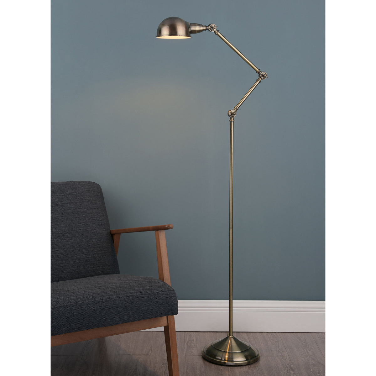 An antique brass floor lamp with an adjustable arm and dome shade stands next to a dark gray armchair.